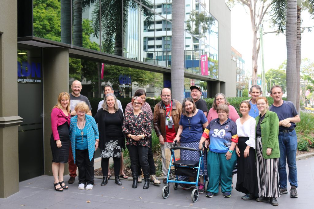 15 Brisbane Hot Topics members standing outside the QDN office, all looking very happy. 