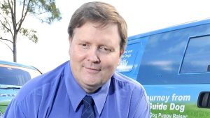 Photo of Paul Larcombe in a blue business shirt smiling at the camera. There is a van behind him.