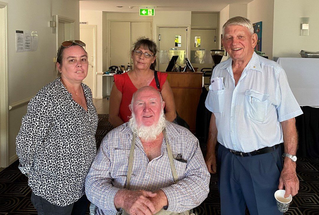 Two women and a man standing around another man in a chair.