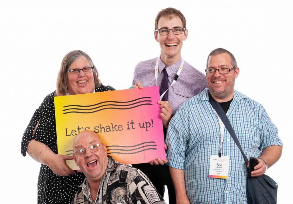 A group of happy smiling people holding a sign saying Let's shake it up!