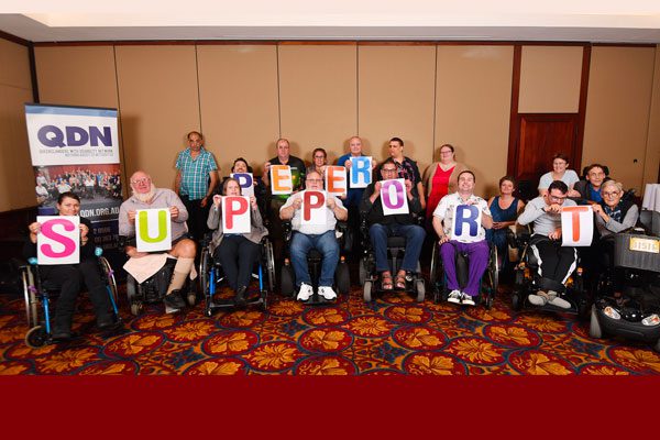 A group of people with disabilities in a room, each holding a letter that together reads Peer Support.