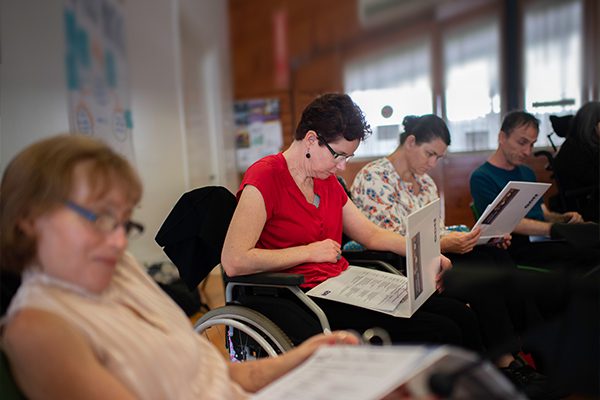 A row of people some in wheelchairs reading information in folders.