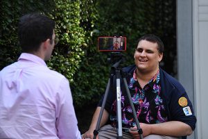 A man being interviewed and recorded on an iphone which is set up on a tripod.