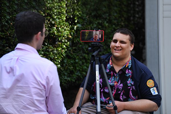 A man being interviewed and recorded on an iphone which is set up on a tripod. width=