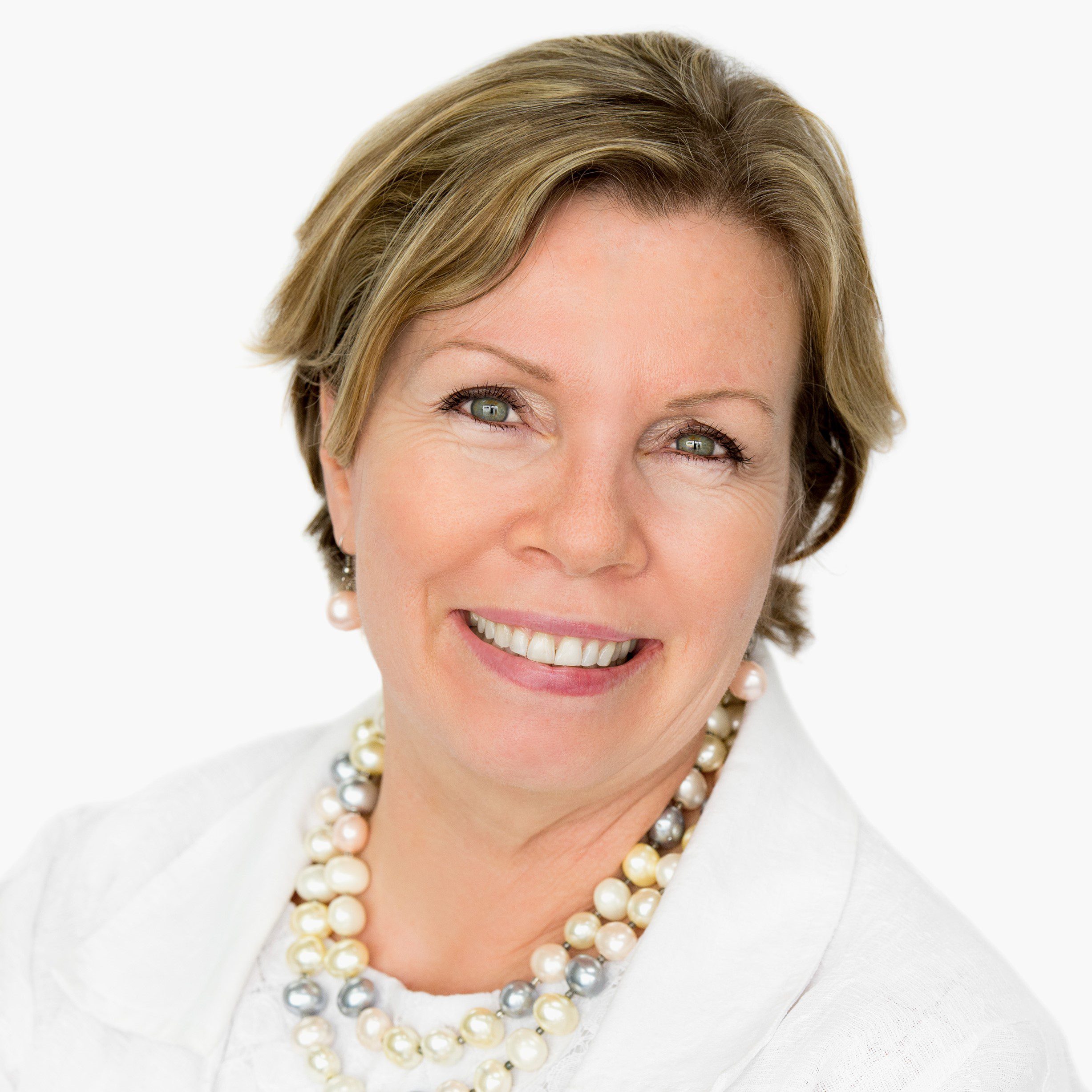 QDN Board member Colleen Papadopoulos, wearing a white shirt and white jacket and necklace, with short light brown hair and smiling at the camera.