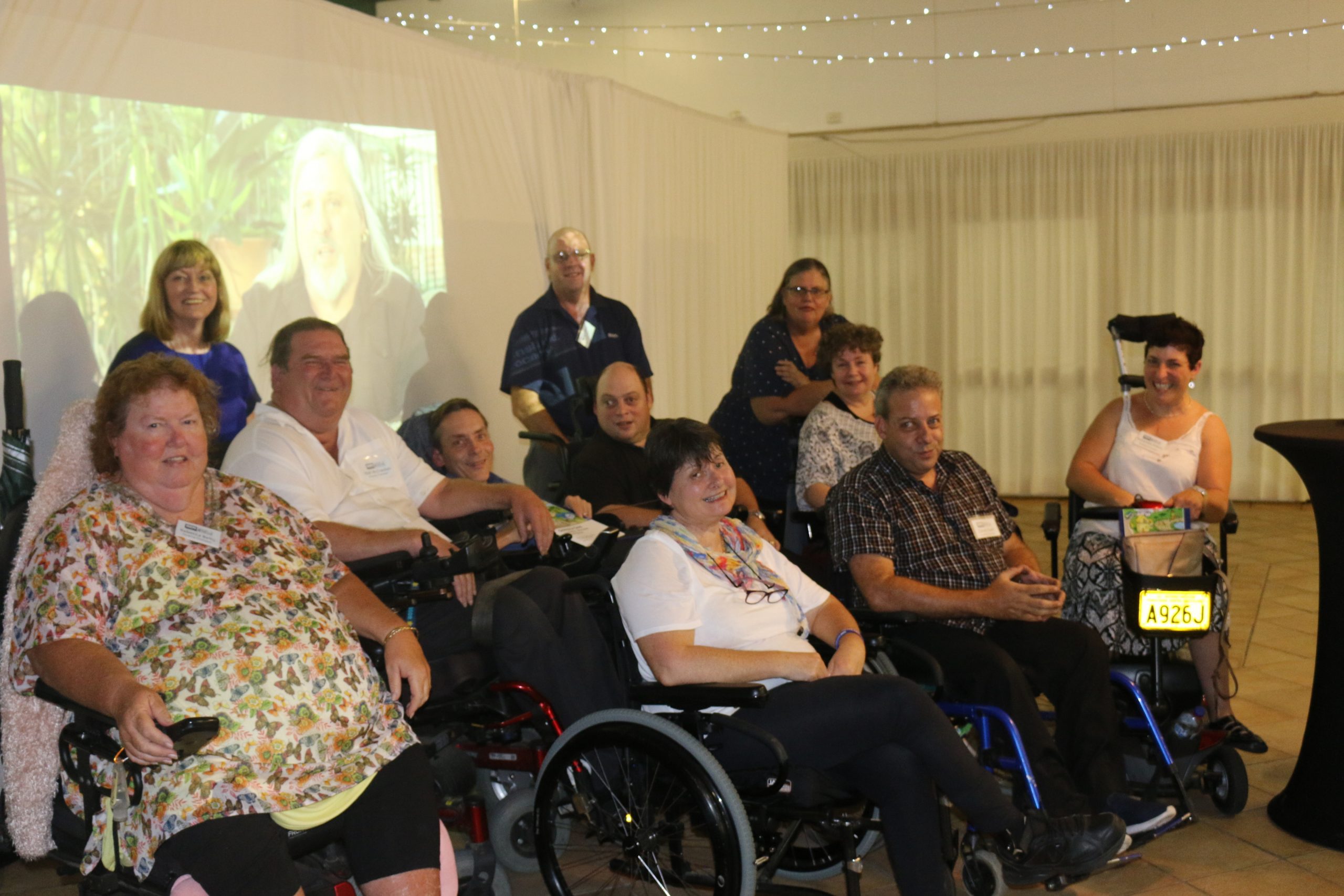 A group of men and women, some standing and some in wheel chairs. All looking at the camera.