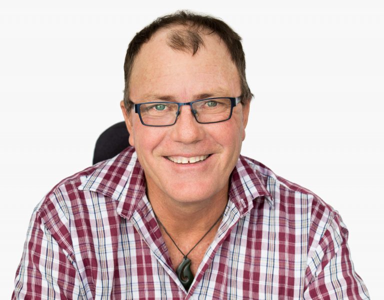 Q D N board member Peter Gurr, wearing glasses and a checkered shirt smiling at camera