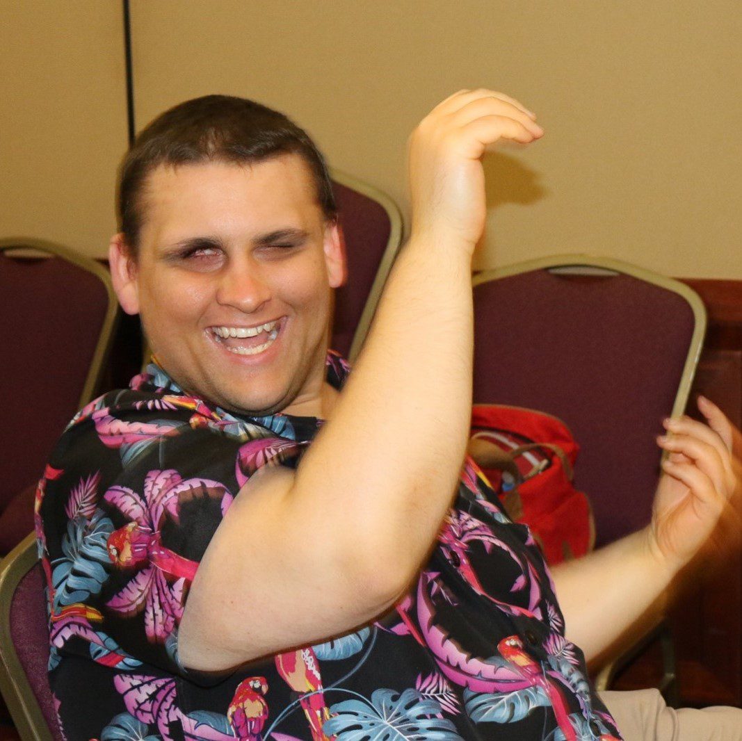 A man sitting in a chair is smiling broadly and is putting his arms up in the air.
