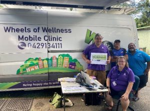 4 people standing by a white van. The van says Wheels of Wellness Mobile Clinic.