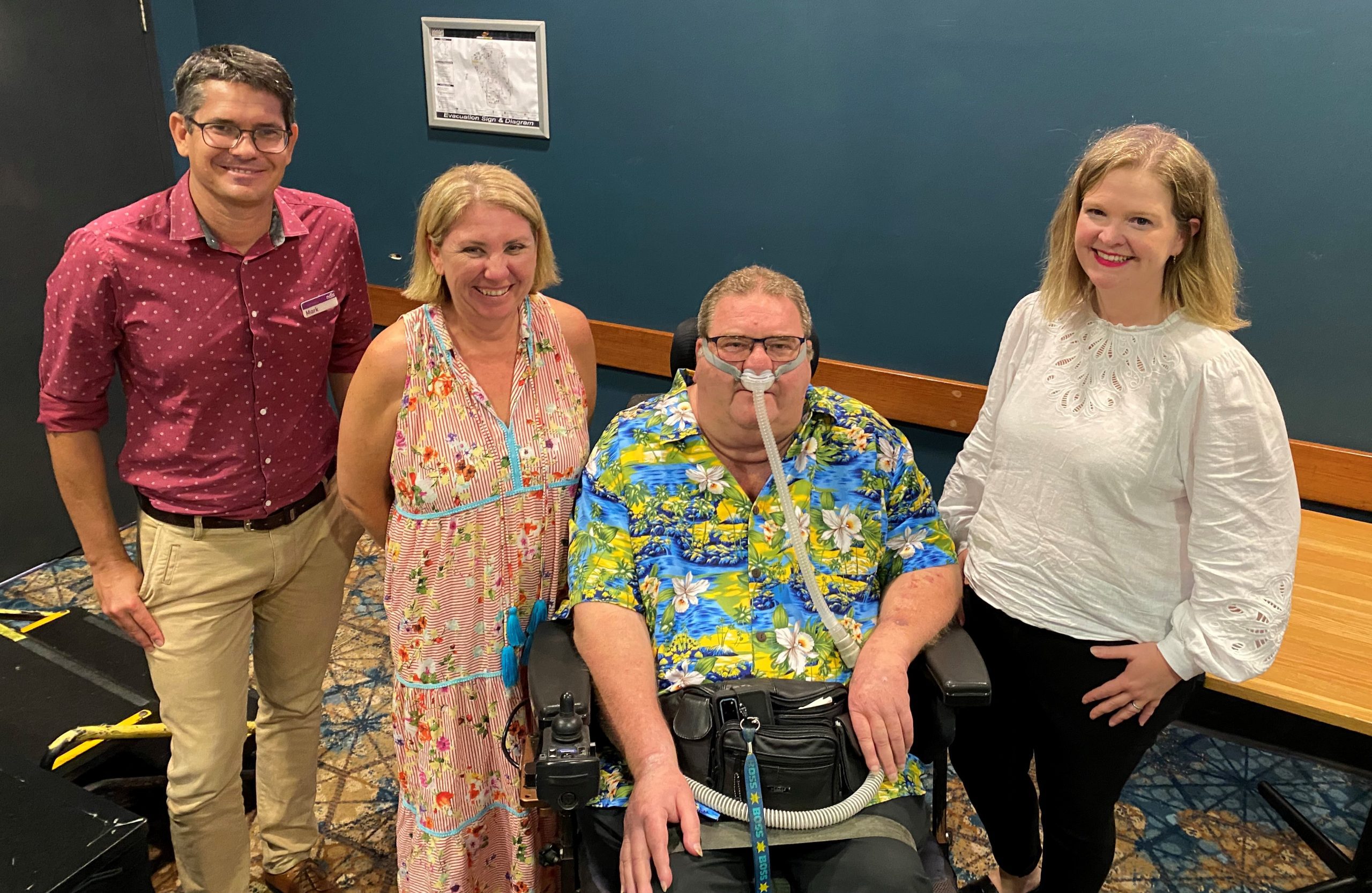 A man and two women standing and a man sitting in a wheelchair, all looking at the camera smiling.