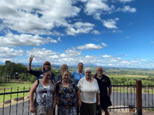 Picture of seven members of QDN Peer Support group at a recent gathering. Also pictured is Paige Armstrong CEO QDN. Picture taken outside with views of green fields and blue sky.