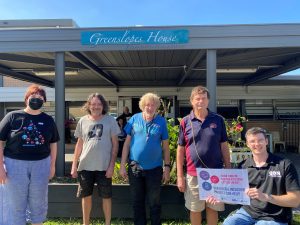 Four people standing and one person sitting in a wheelchair, outside the Greenslopes House entrance