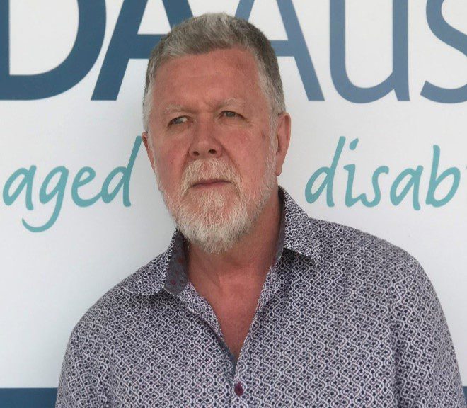 A man with short grey hair and a beard, wearing a buttoned up business shirt.