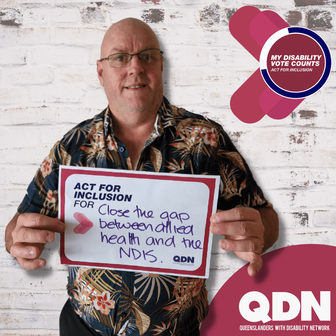 A man wearing a floral shirt holding a sign that says Act for inclusion for and written in pen "Close the gap between allied health and the NDIS. My disability vote counts, Act for inclusion". QDN Queenslanders with Disability Network.