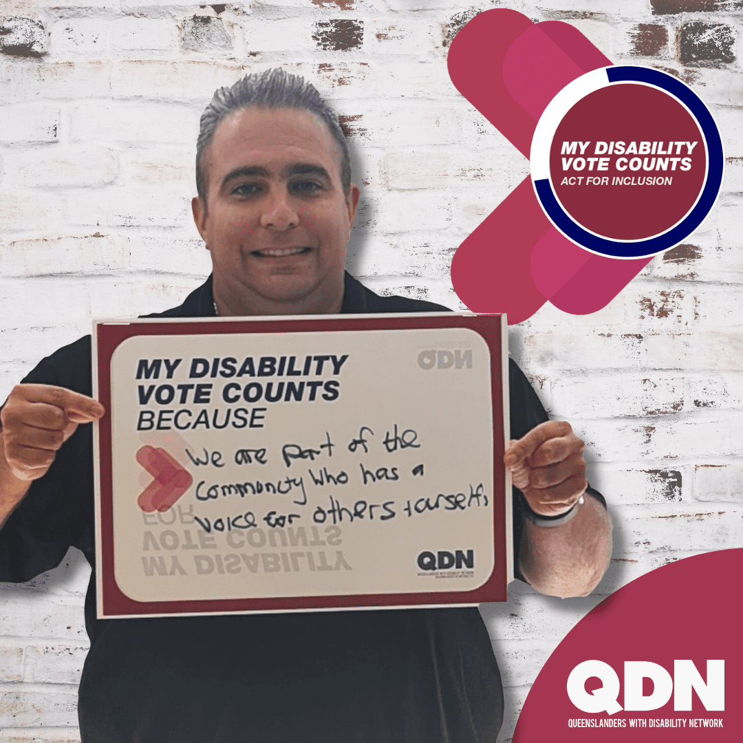 A man in a black shirt and short dark hair, smiling at the camera and holding up a sign that says My Disability vote counts because… then handwritten it says “We are part of the community who has a voice for others and ourselves”. There is a QDN logo in the bottom right – Queenslanders with Disability Network. In the top right there is a circle icon with the text My Disability Vote Counts – Act for Inclusion. 