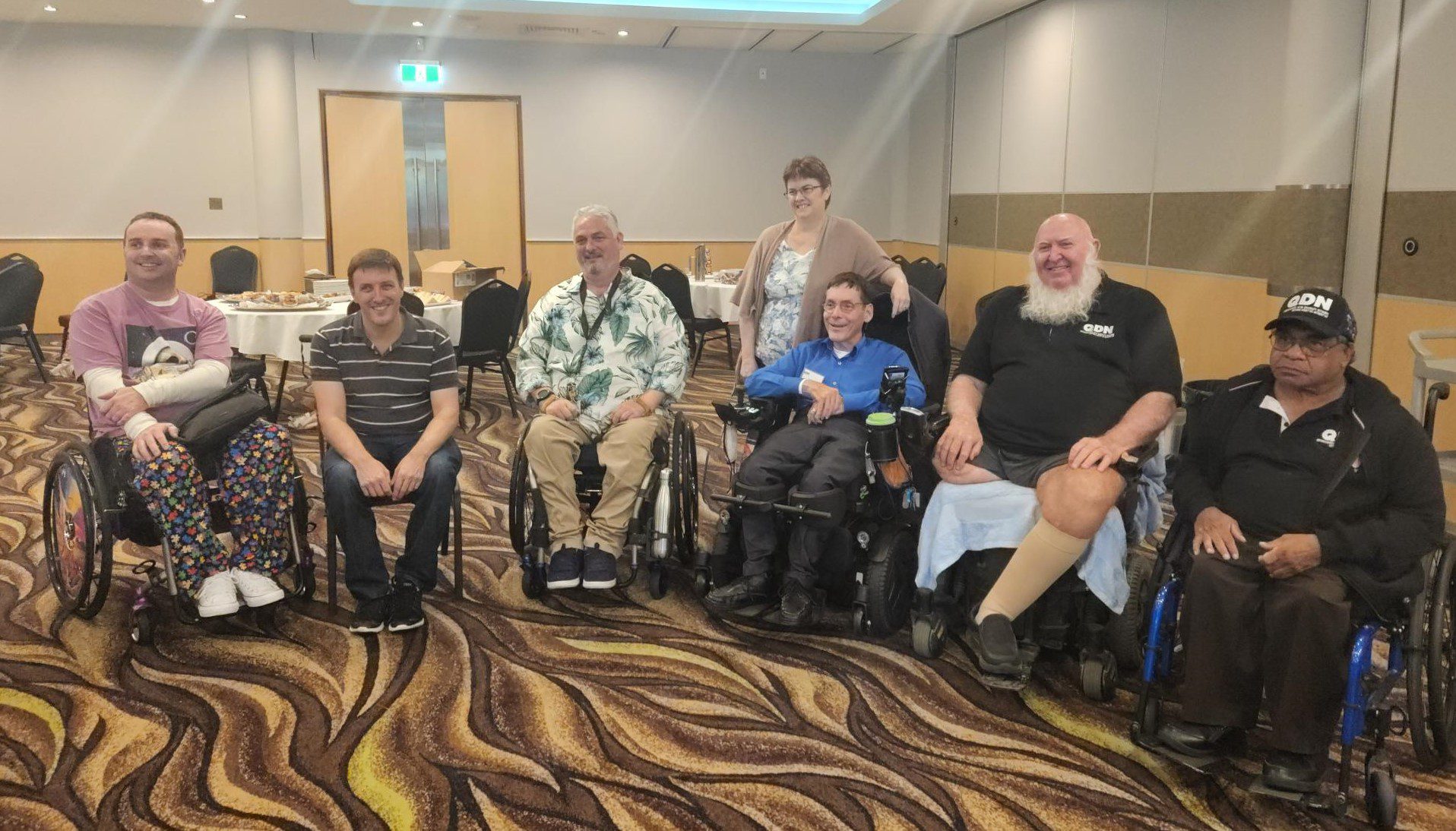 A group of people, some sitting in chairs, some in sitting in wheelchairs and one woman standing.