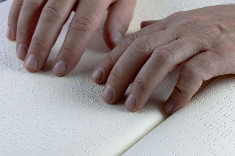 A close up photo of someone using their fingertips to read Braille from a page of a book that is written in Braille.