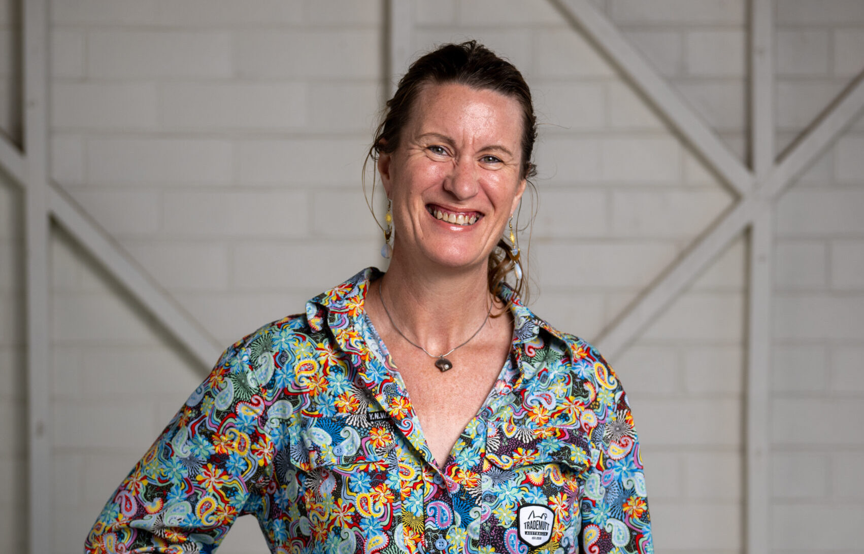 A woman with a ponytail, wearing a floral T-shirt, is smiling in front of a plain white background.