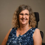 Woman in a wheelchair, wearing glasses and a blue dress