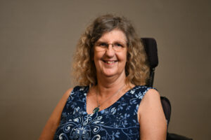 Woman in a wheelchair, wearing glasses and a blue dress