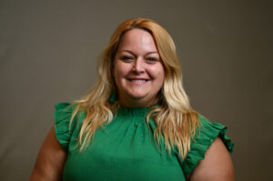 Woman with shoulder length blonde hair and wearing a green dress