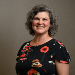 A woman with curly hair and a black dress with colourful pictures on it.