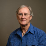 Man with short hair and a blue shirt. Also wearing glasses.