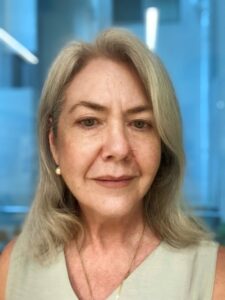Woman with blonde hair and wearing a green top and a necklace