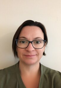 Victoria has a very short brown hair and is wearing dark blue reading glasses