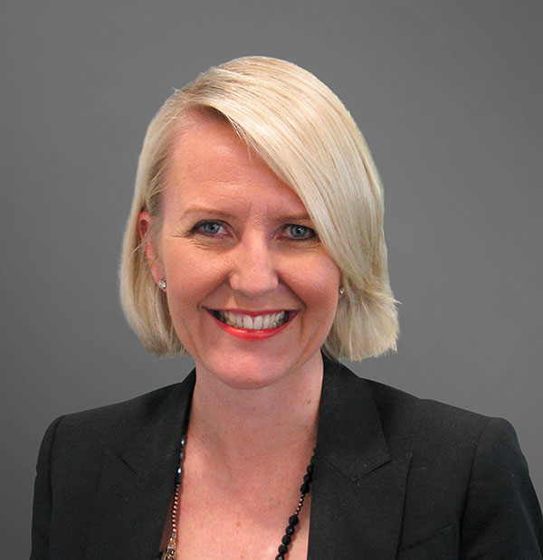 Woman with medium blonde hair and a black jacket smiling at the calendar.