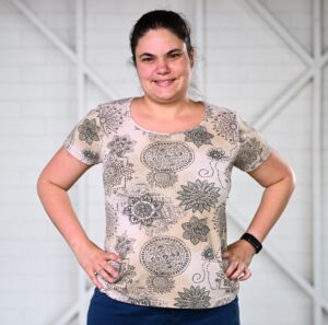Picture of a woman standing in front of a white wall, with her hands on her hips, smiling at the camera.