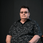 A man wearing a dark short sleeved shirt and sun glasses