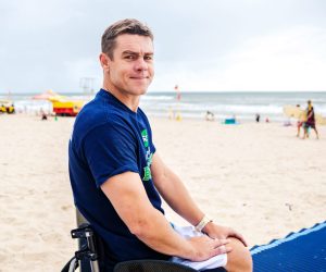Ben is at the beach in his wheelchair. He looks back at the camera.