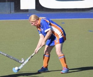 Kim plays hockey on the green astro turf. Her uniform is blue and orange.