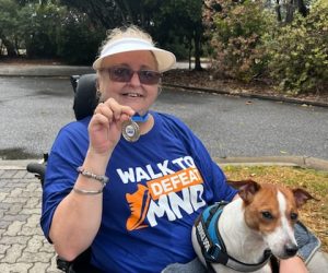 Image: Carmen Jen, a QDN member and 2024 Emerging Leader, sits in her wheelchair holding her MND Cornflower Spirit Award. A dog sits beside her.